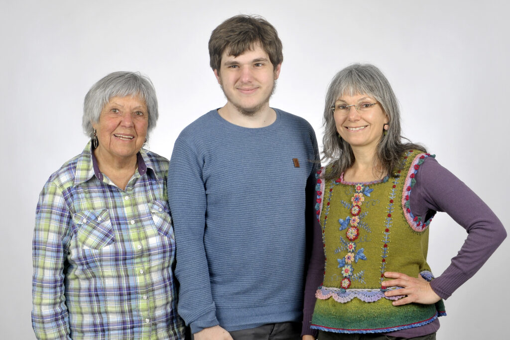 A lady in her 70s, a 19 year old person and a woman in her 50s wearing very colorful clothes in a photo studio